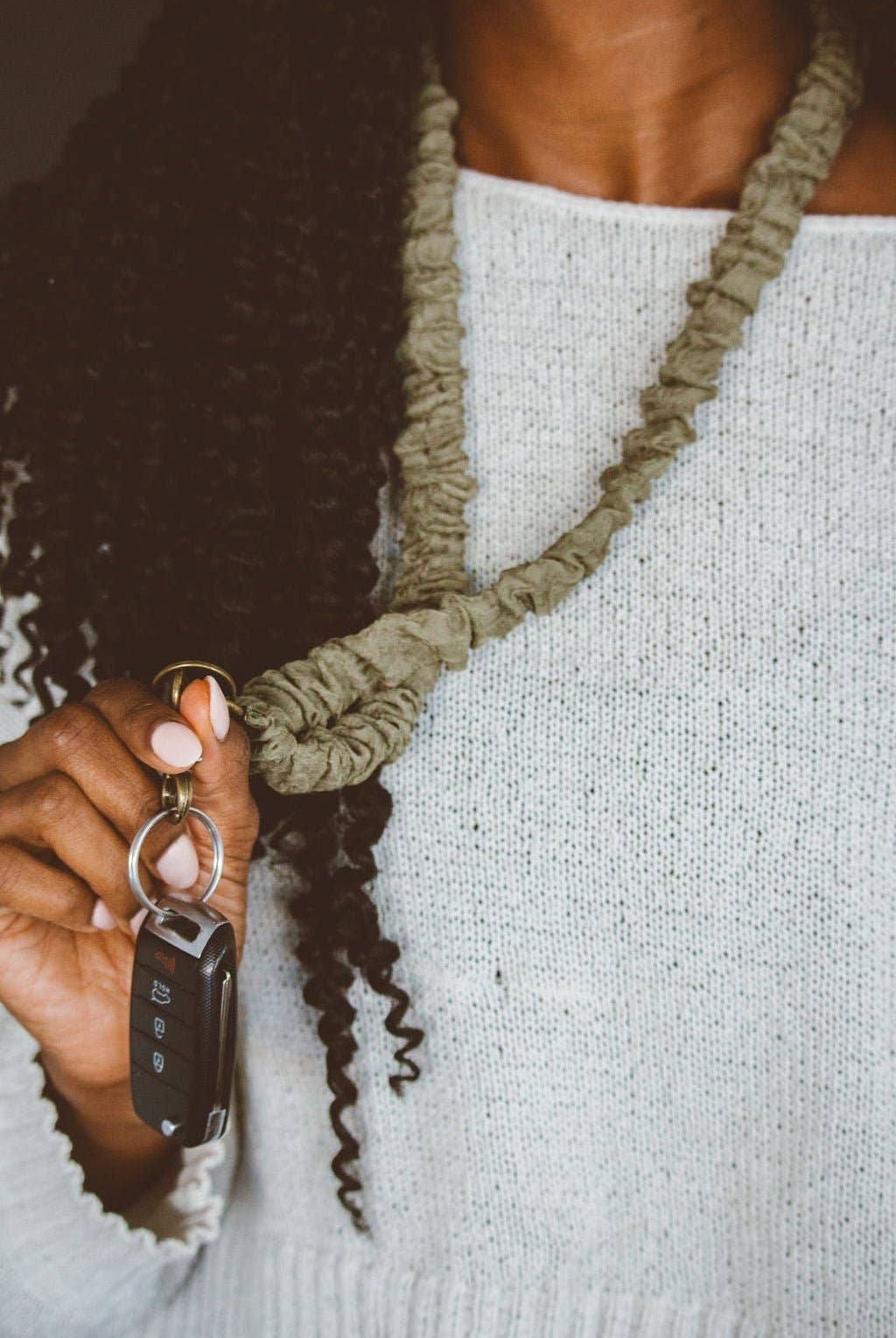 A person holding keys attached to a moss green colored crinkled fabric lanyard.