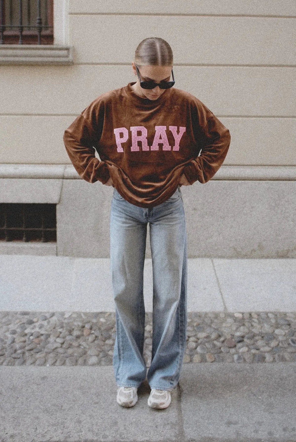 Brown velvet sweatshirt featuring pink "PRAY" text across the chest, styled with light wash jeans.