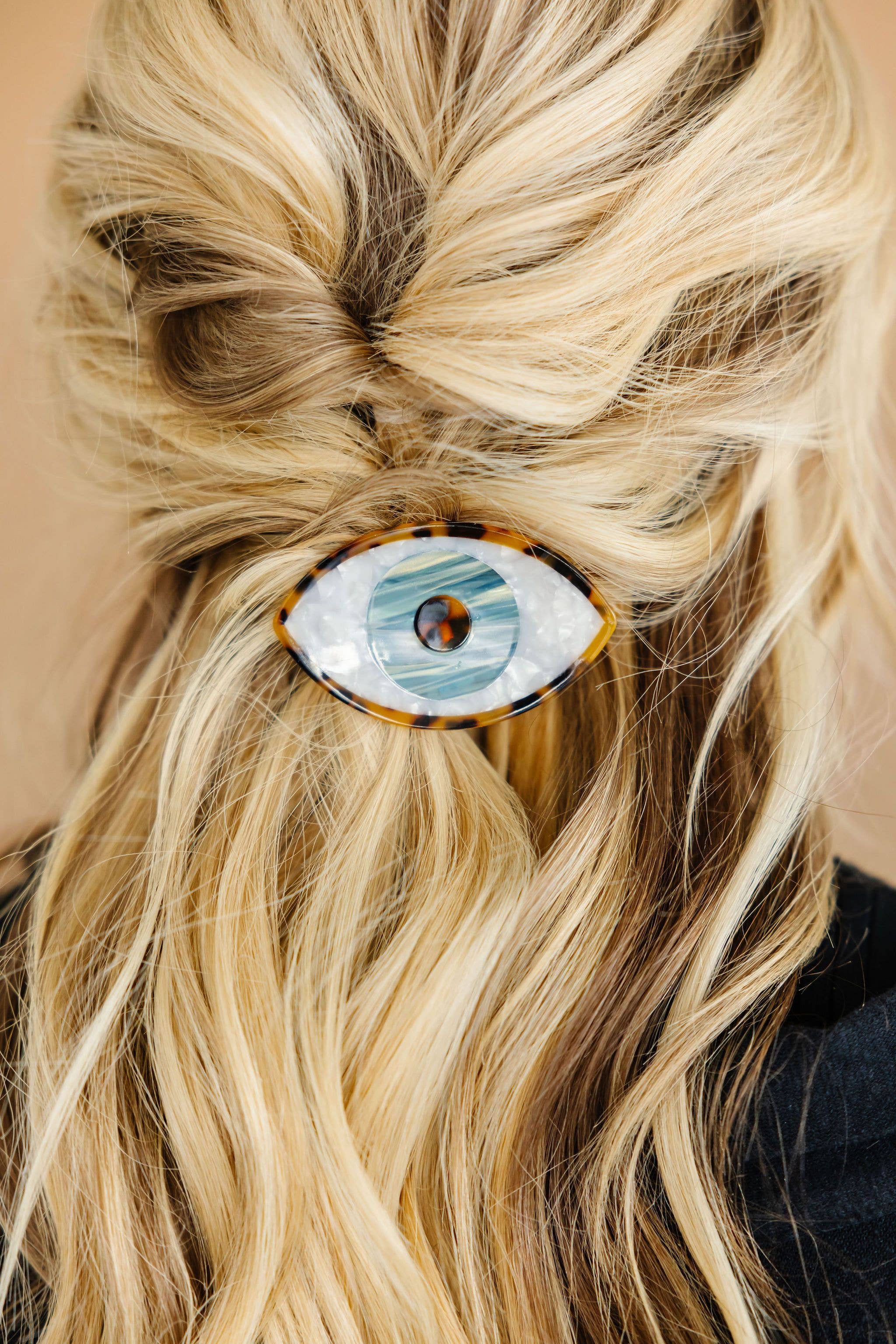 A person with blonde hair has their hair styled with a medium-sized claw clip that has a spooky eye design.
