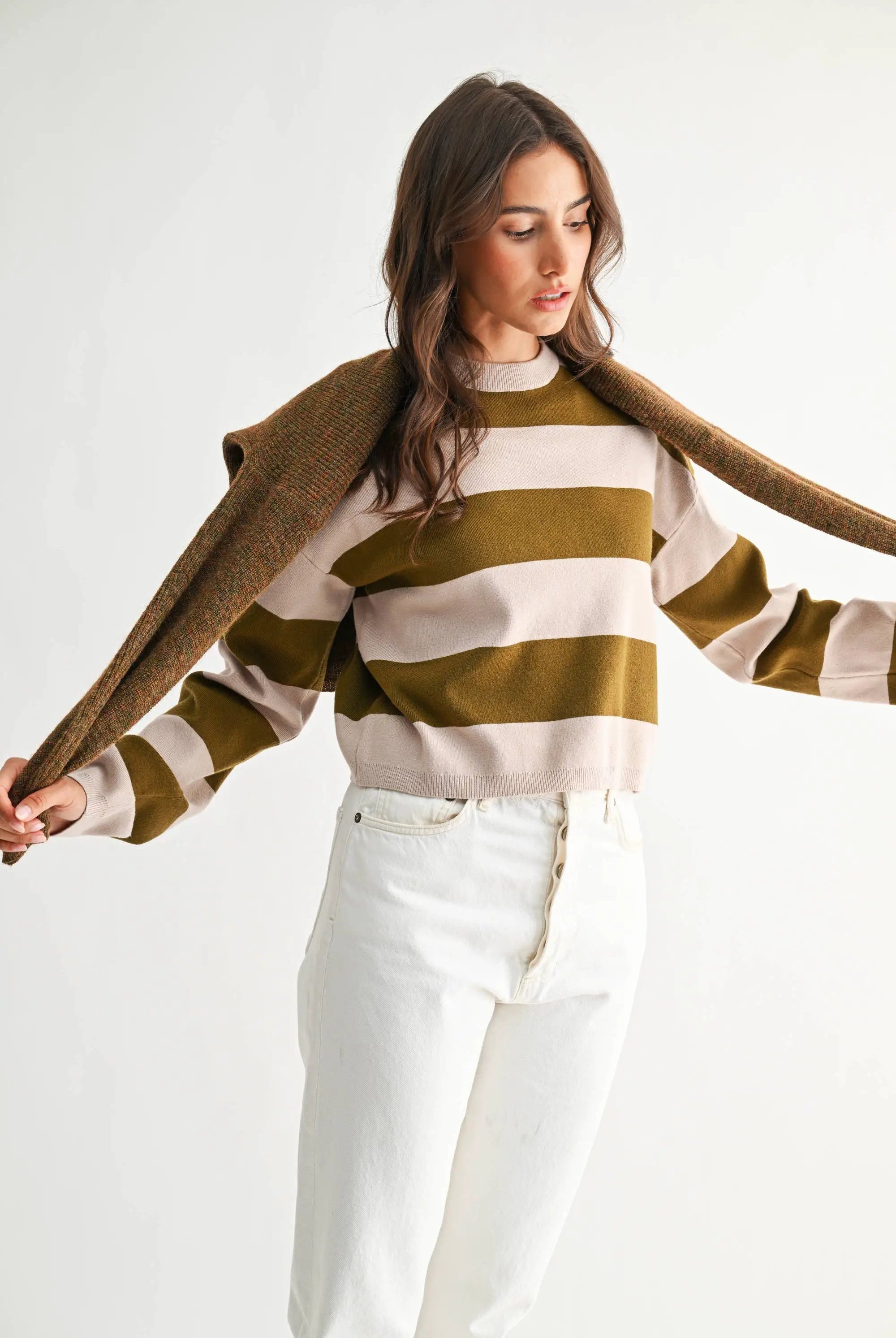 Model wearing a light taupe and olive bold stripe crewneck sweater with cream bands, relaxed fit.