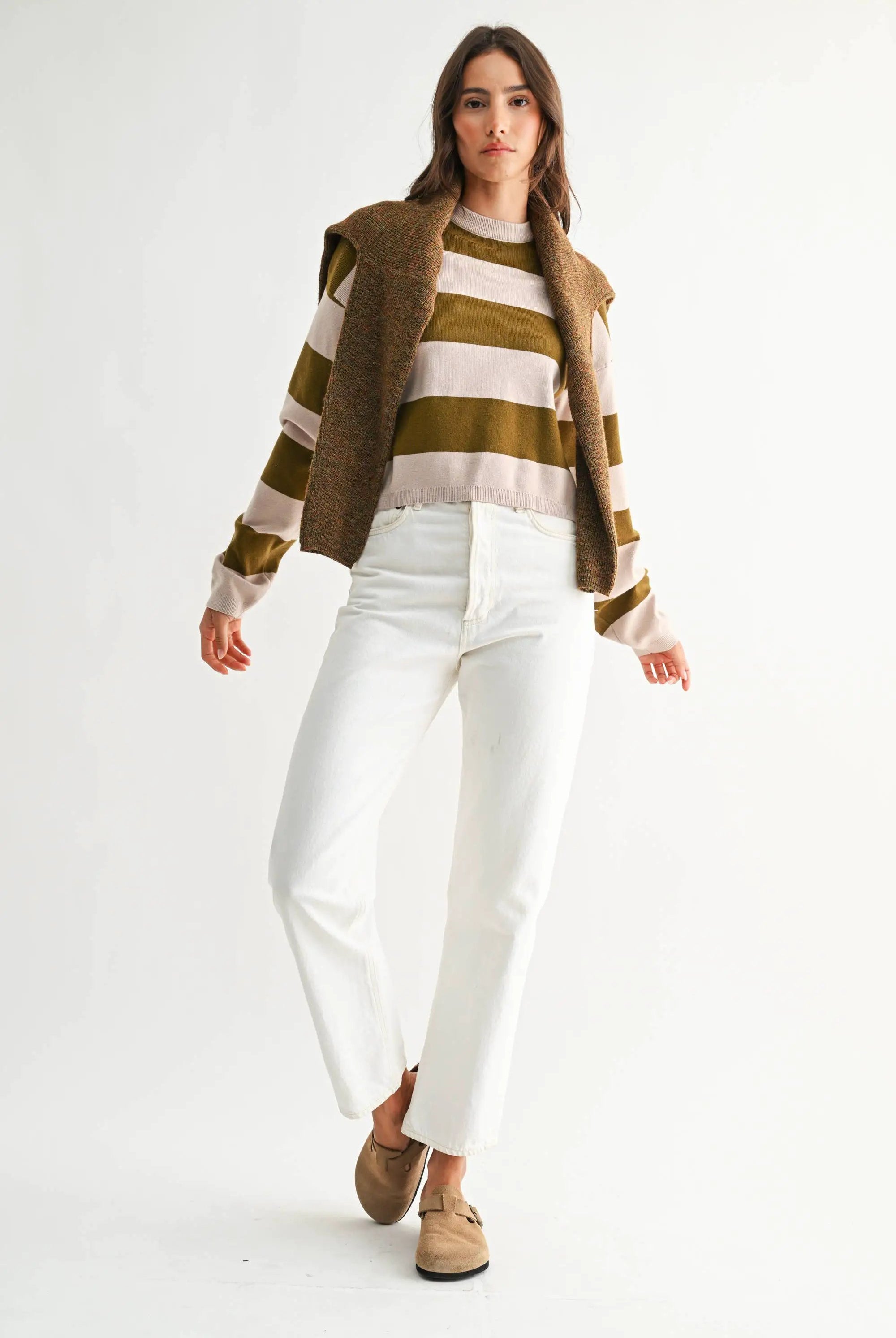 Model wearing light taupe and olive bold stripe crewneck sweater with relaxed fit and white jeans.