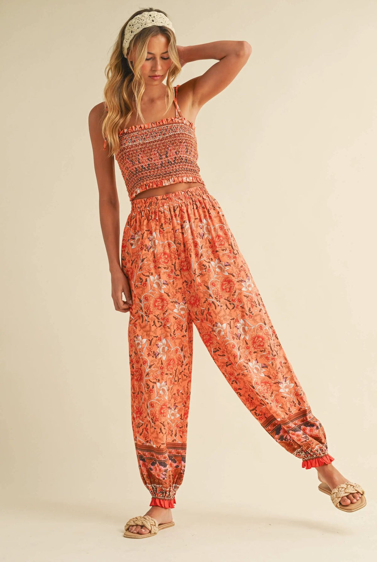 Woman wearing a coordinated orange floral two-piece set with a smocked crop top and high-waisted boho pants.