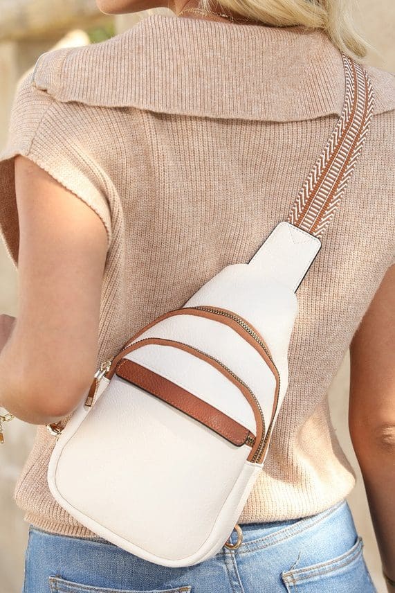 A woman wearing a white purse with brown straps.
