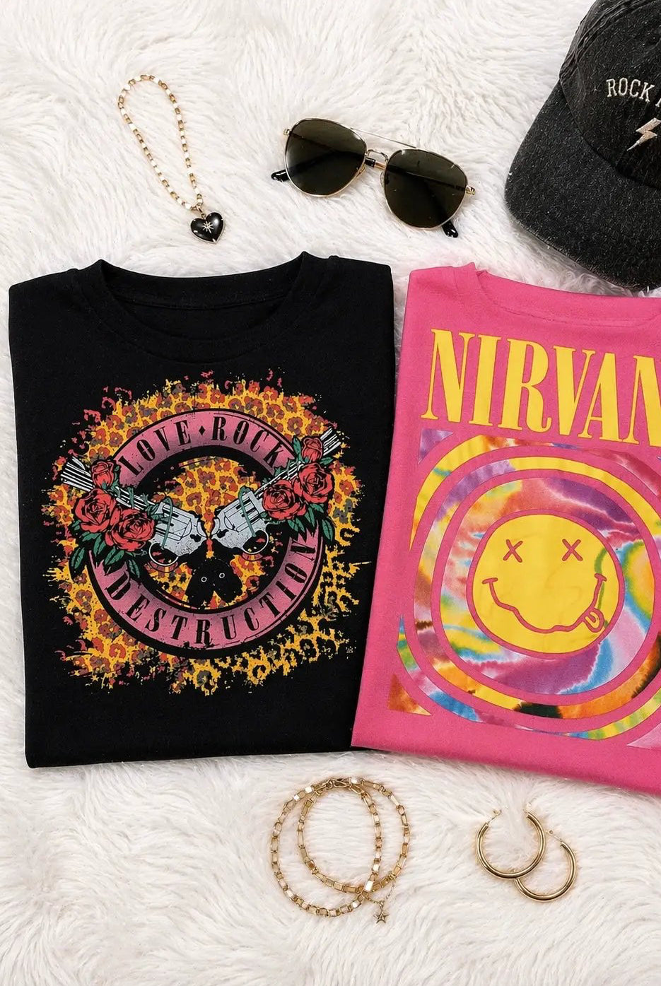 Pink Nirvana graphic tee with tie-dye smiley face displayed alongside a black rock print shirt and accessories for a grunge aesthetic.