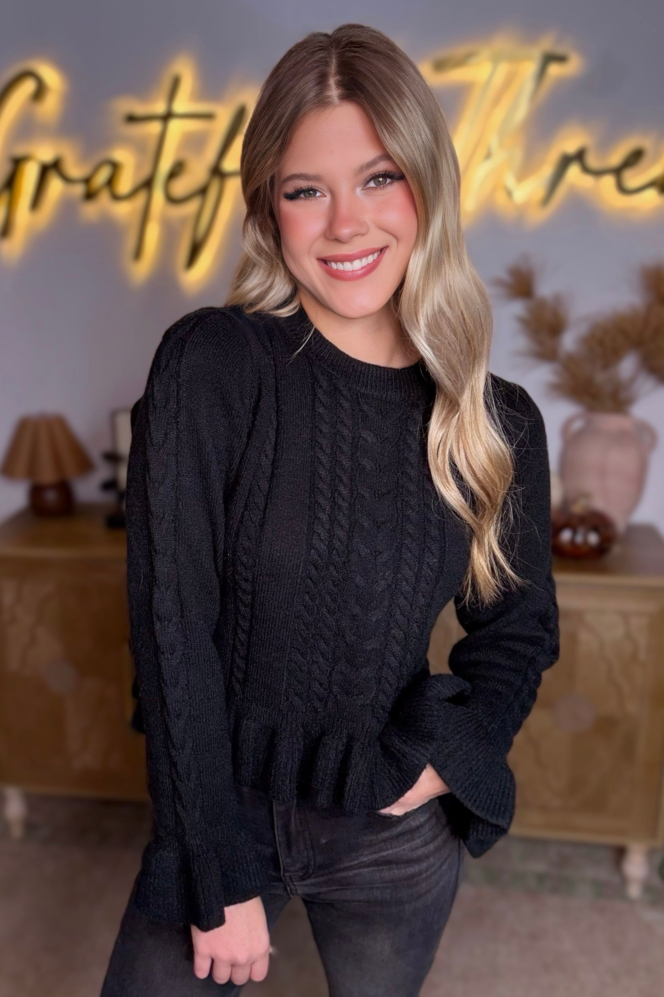 Woman wearing a black sweater standing in front of a decorative backdrop with 'Grateful' text.