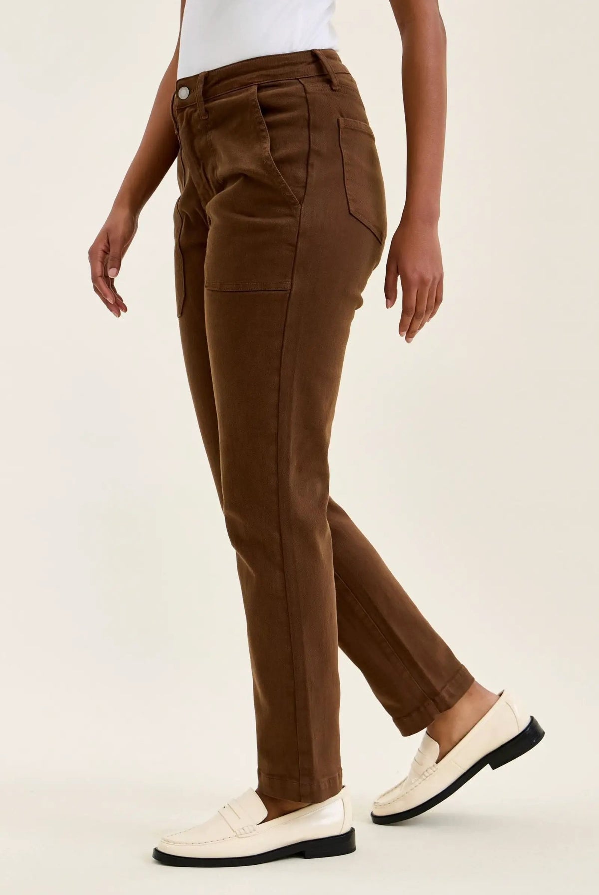 High-waist mahogany stretch jeans with slim straight leg, tailored fit, and double-rolled cuff paired with white loafers.