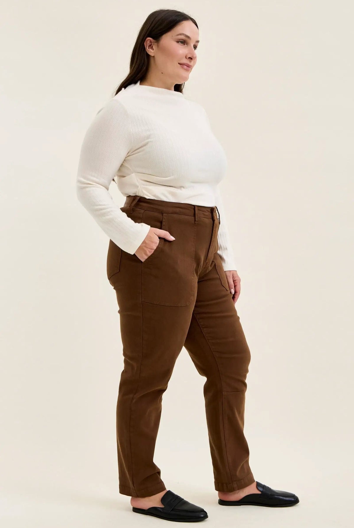 Plus-size model wearing mahogany high-waist stretch jeans with utility pockets and slim-straight legs, styled with a white top and black loafers.