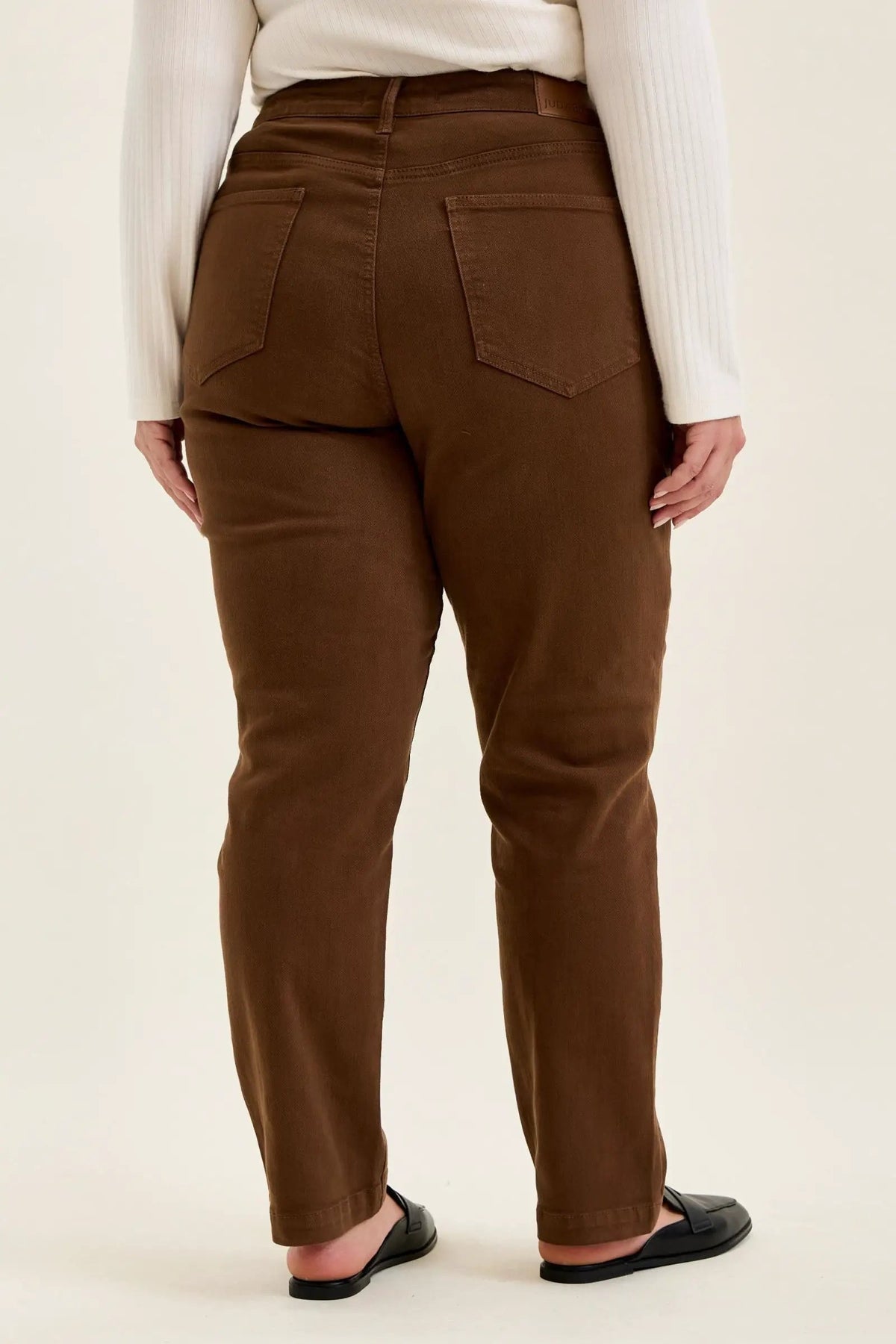 Back view of mahogany high-waist plus stretch jeans with utility pockets and slim-straight legs, styled with black loafers.