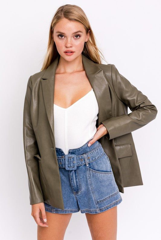 Woman in olive blazer and denim shorts.