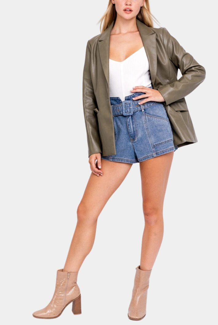 Woman in olive blazer, denim shorts, boots.