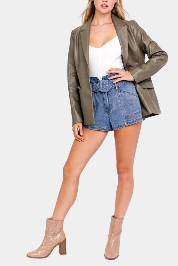 Woman in olive blazer, denim shorts, boots.