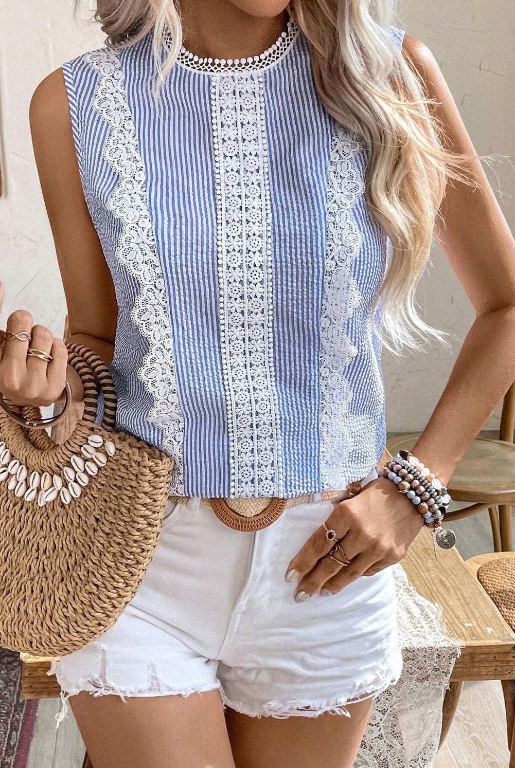 Woman wearing a blue and white striped sleeveless top with lace details, holding a straw bag.