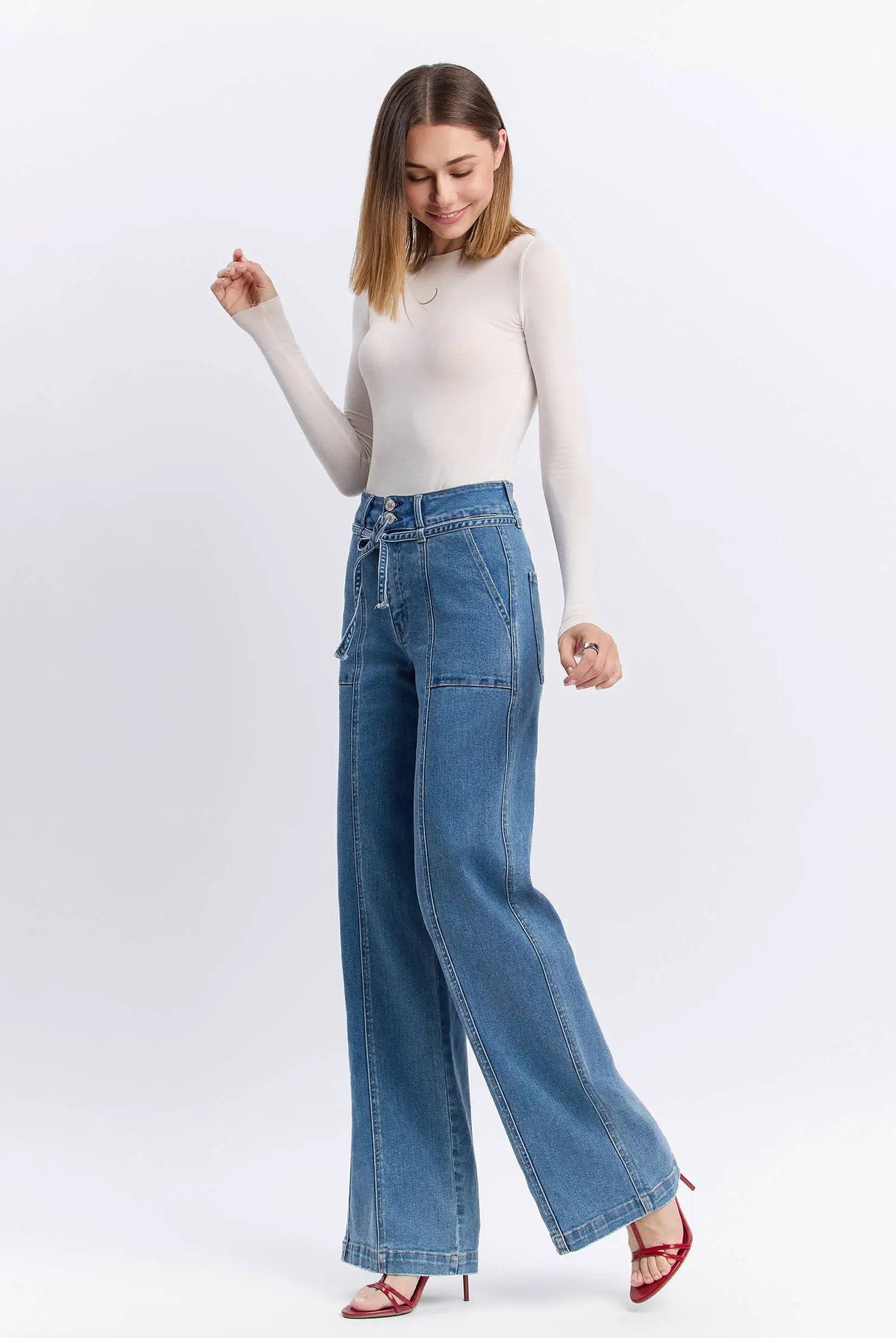 Model in super high rise tie waistband wide leg jeans paired with a cream long sleeve top and red heels, showing off the full-length fit and flattering silhouette.