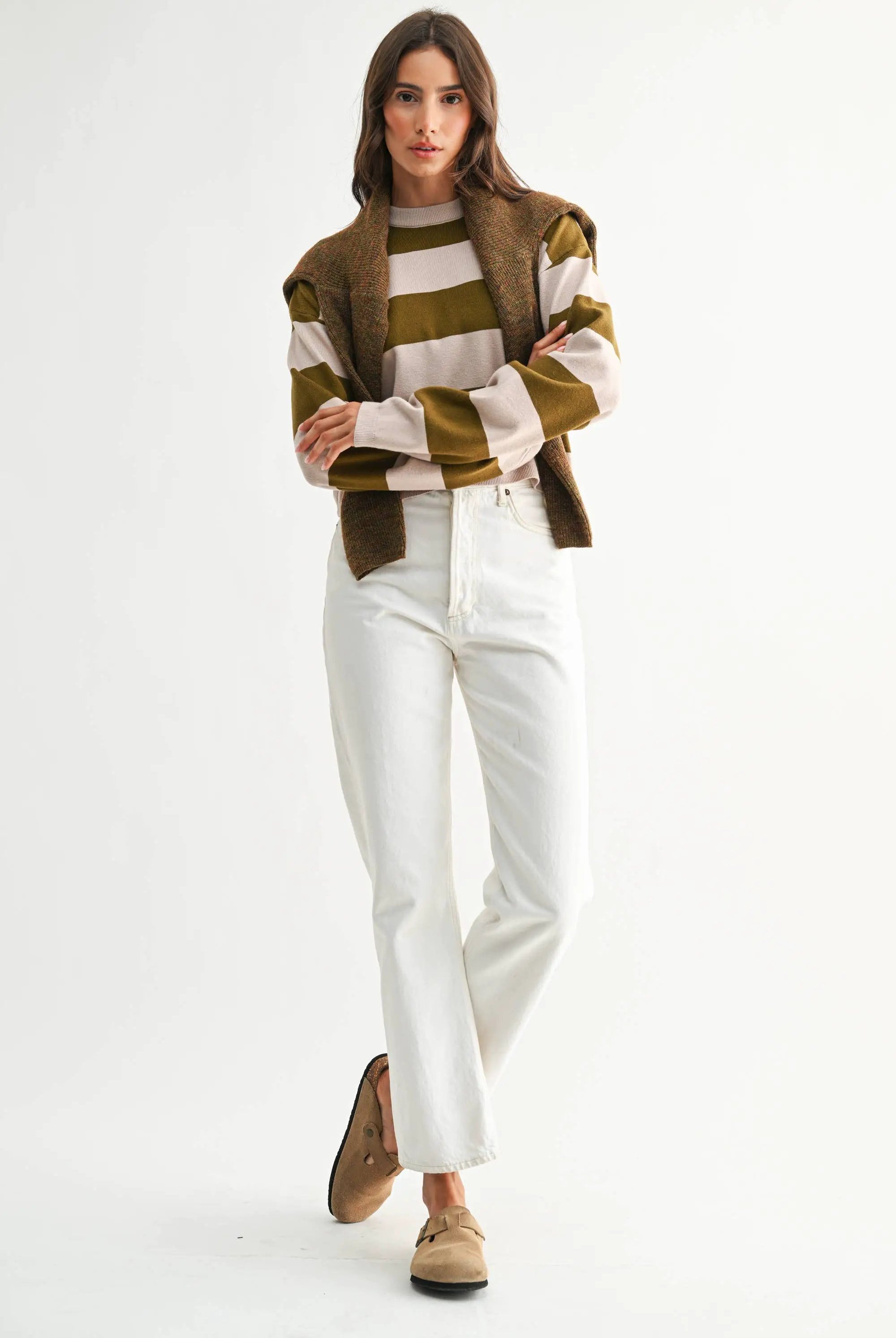 Model wearing taupe and olive bold stripe crewneck sweater with cream stripes, paired with white jeans.
