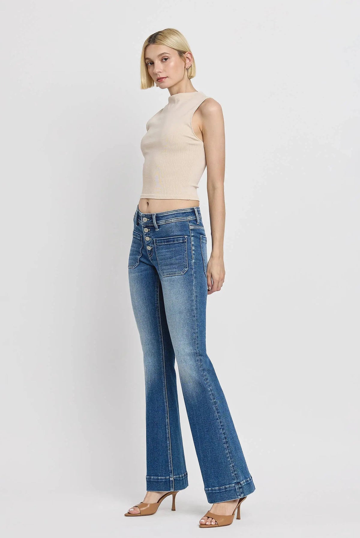 Model wearing the Vervet Alison Mid Rise Flare Jeans with a button fly, high-rise waist, cuffed hem, and patch pockets in a blue denim shade.