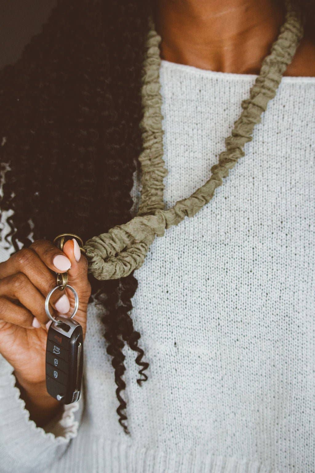 A person holding keys attached to a moss green colored crinkled fabric lanyard.