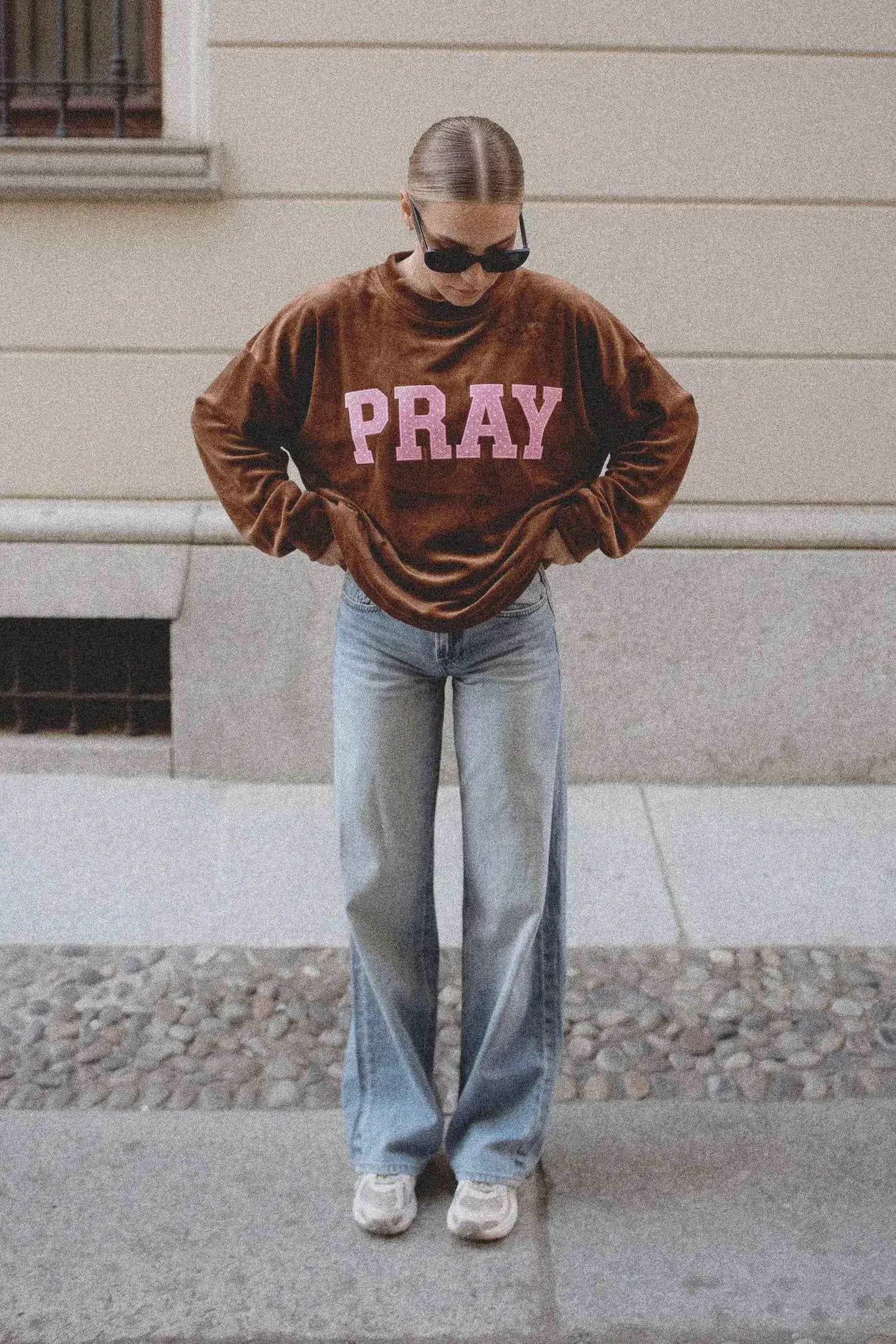 Brown velvet sweatshirt featuring pink "PRAY" text across the chest, styled with light wash jeans.