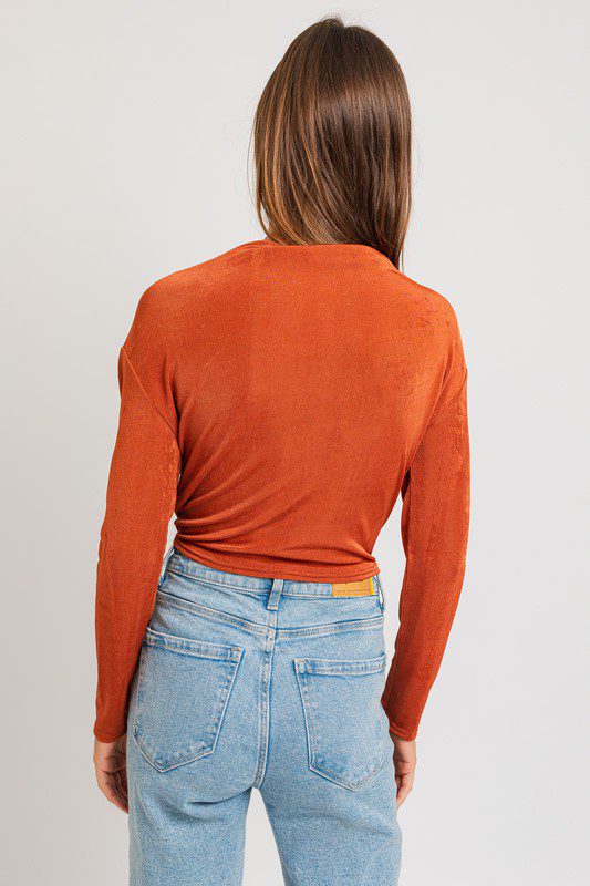 Here's an alt tag for the image: Woman in burnt orange long sleeve top and jeans.