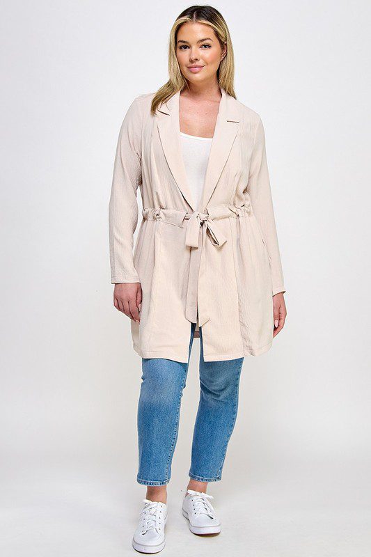 Beige belted jacket with jeans and sneakers.