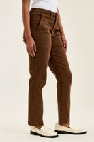 High-waist mahogany stretch jeans with slim straight legs, featuring knee darts and a double-rolled cuff for a tailored fit.