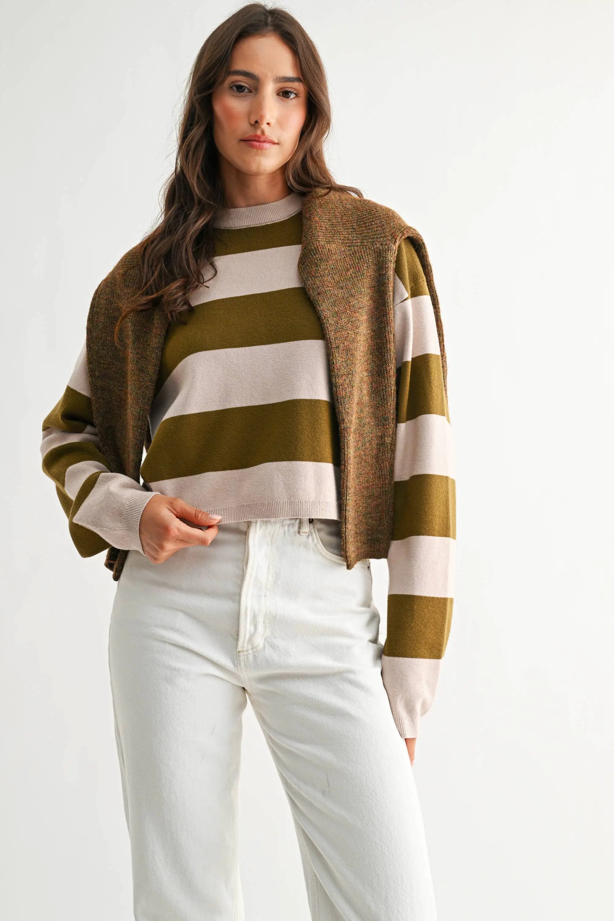Model wearing light taupe and olive bold stripe crewneck sweater with a brown knit cardigan draped over shoulders.