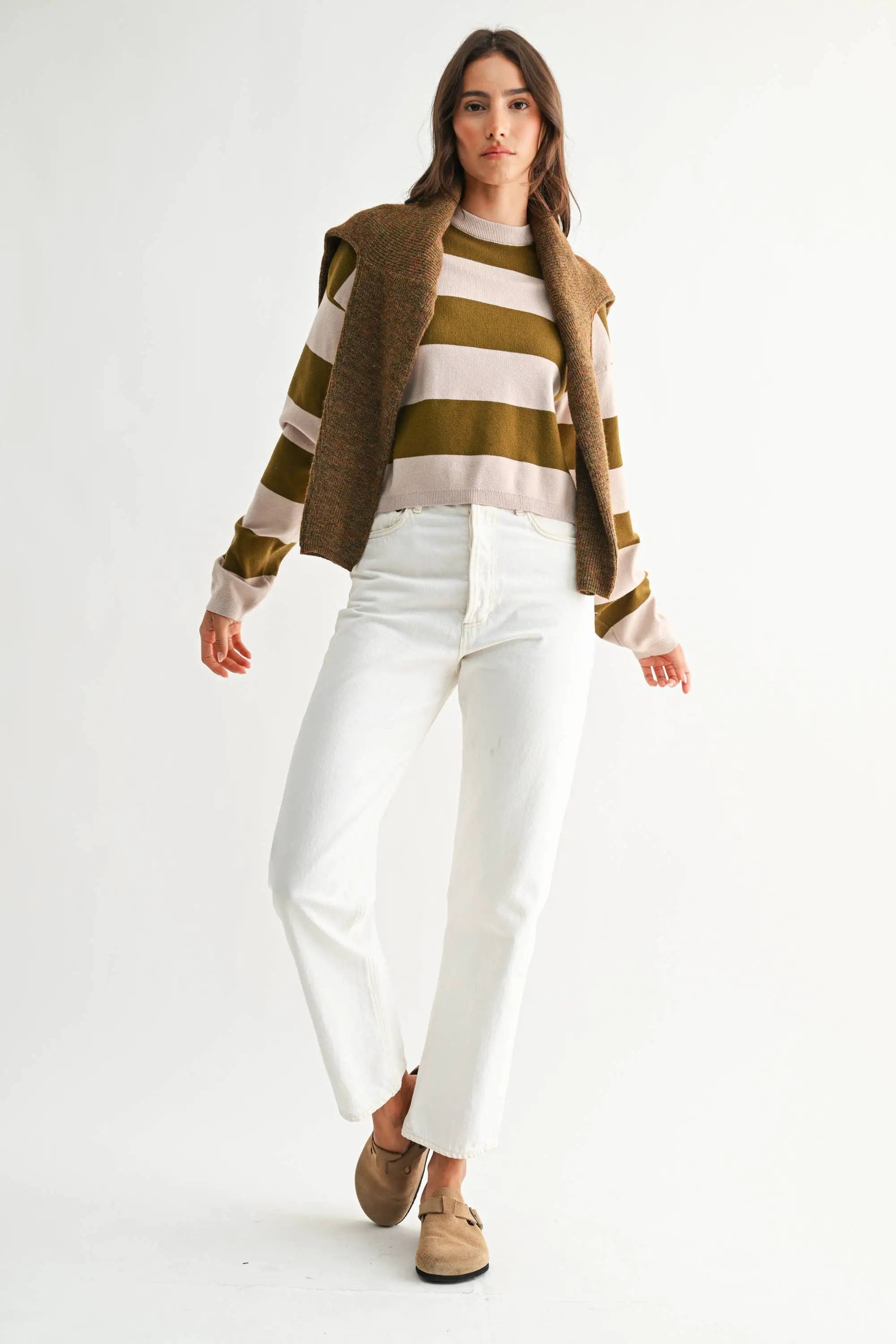 Model wearing light taupe and olive bold stripe crewneck sweater with relaxed fit and white jeans.