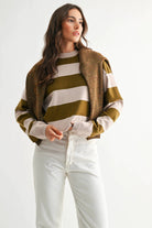 Model wearing light taupe and olive bold stripe crewneck sweater with cream stripes and brown textured cardigan.