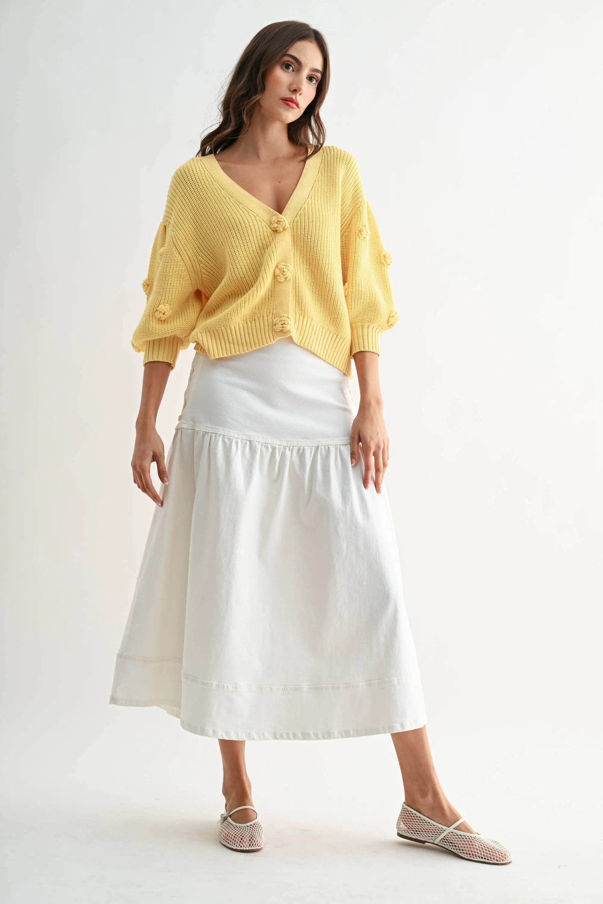 LT.YELLOW textured knit cardigan with 3D floral buttons and relaxed fit, styled over a white skirt.