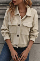 A woman sitting on the ground wearing a beige jacket.