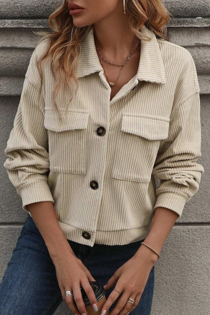 A woman sitting on the ground wearing a beige jacket.