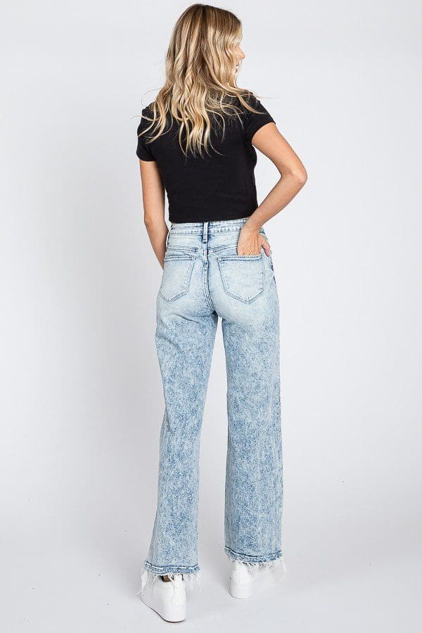 A woman wearing jeans and black shirt standing next to a wall.