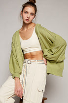 Woman in olive green cardigan and cream pants.