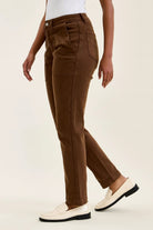 High-waist mahogany stretch jeans with slim straight leg, tailored fit, and double-rolled cuff paired with white loafers.