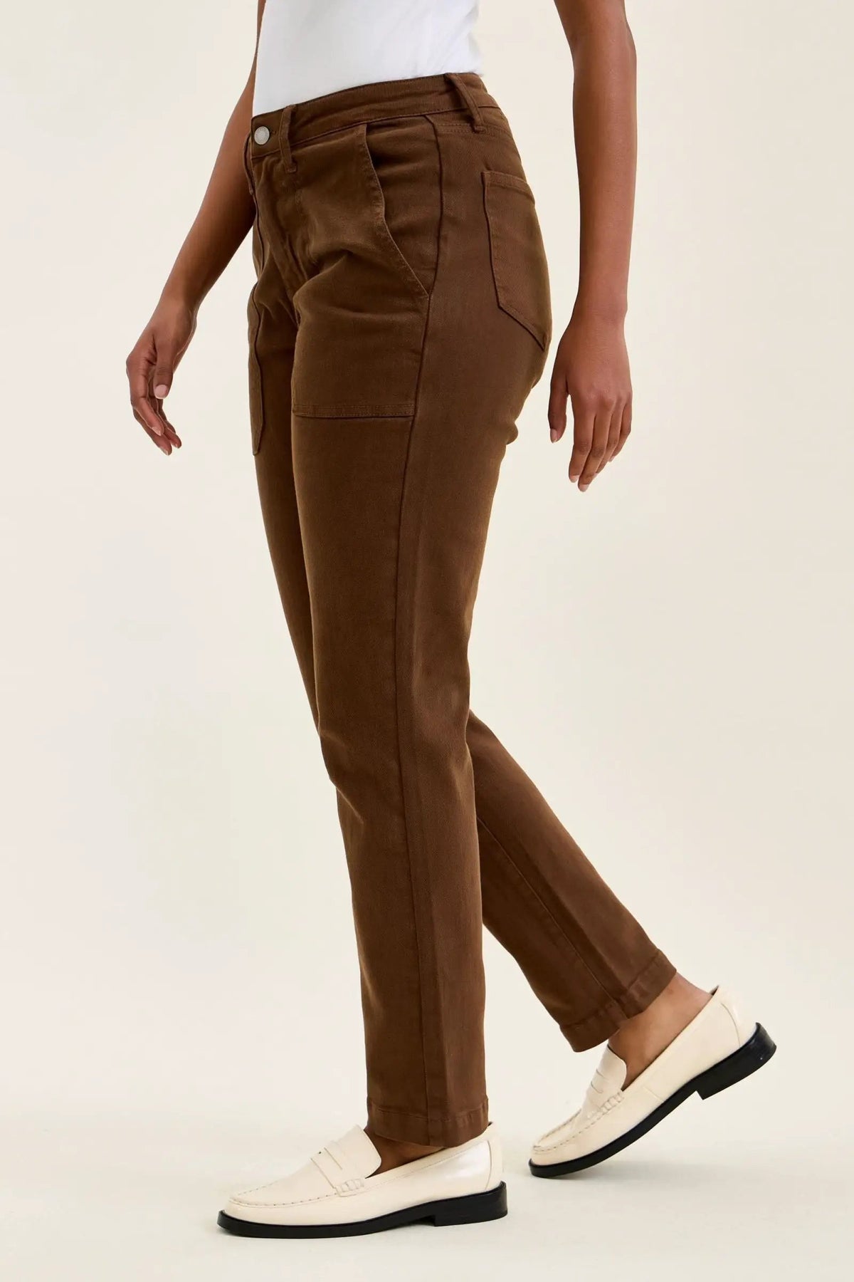 High-waist mahogany stretch jeans with slim straight leg, tailored fit, and double-rolled cuff paired with white loafers.