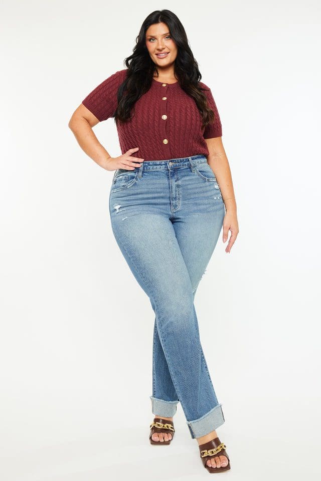 A woman standing in front of a wall wearing jeans.