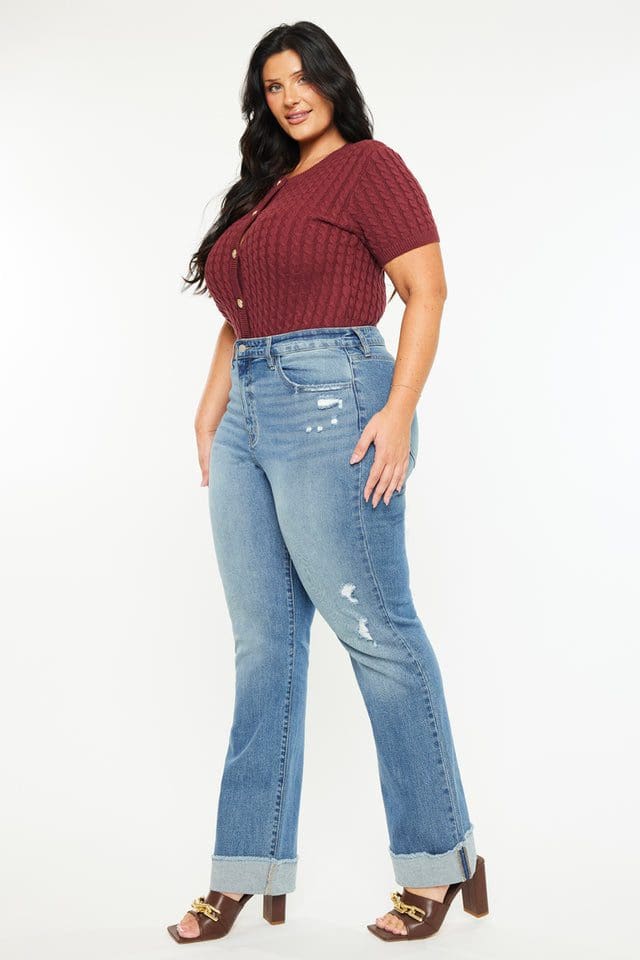 A woman standing in front of a wall wearing jeans.