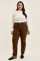 Plus size model wearing mahogany high-waist stretch jeans with utility pockets and slim-straight leg in double-rolled cuffs.