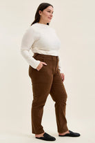 Plus-size model wearing mahogany high-waist stretch jeans with utility pockets and slim-straight legs, styled with a white top and black loafers.
