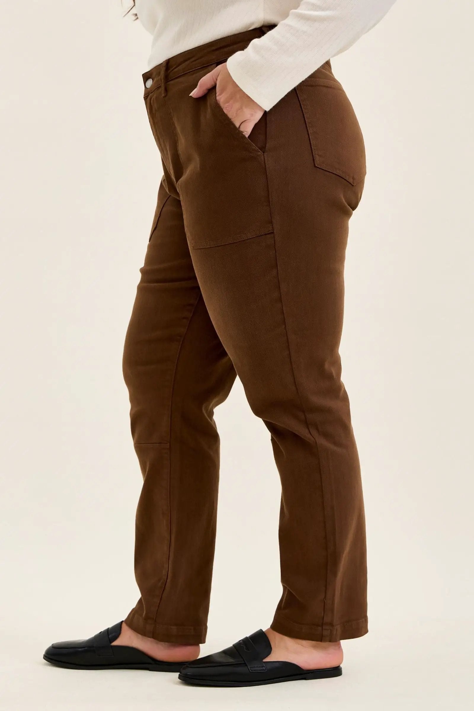 Side view of mahogany high-waist plus stretch jeans featuring utility pockets, slim-straight legs, and rolled cuffs worn with black loafers.