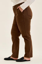 Side view of mahogany high-waist plus stretch jeans featuring utility pockets, slim-straight legs, and rolled cuffs worn with black loafers.