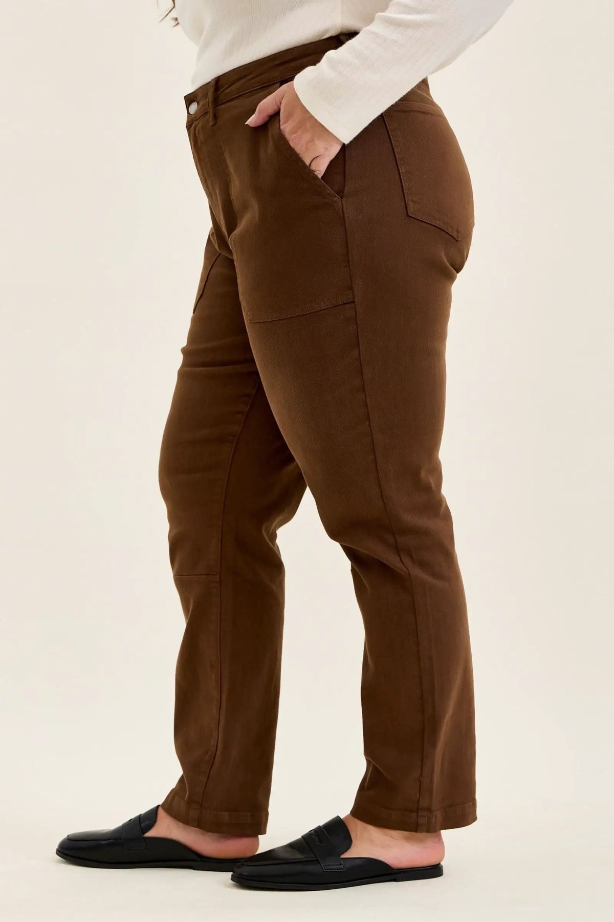 Side view of mahogany high-waist plus stretch jeans featuring utility pockets, slim-straight legs, and rolled cuffs worn with black loafers.