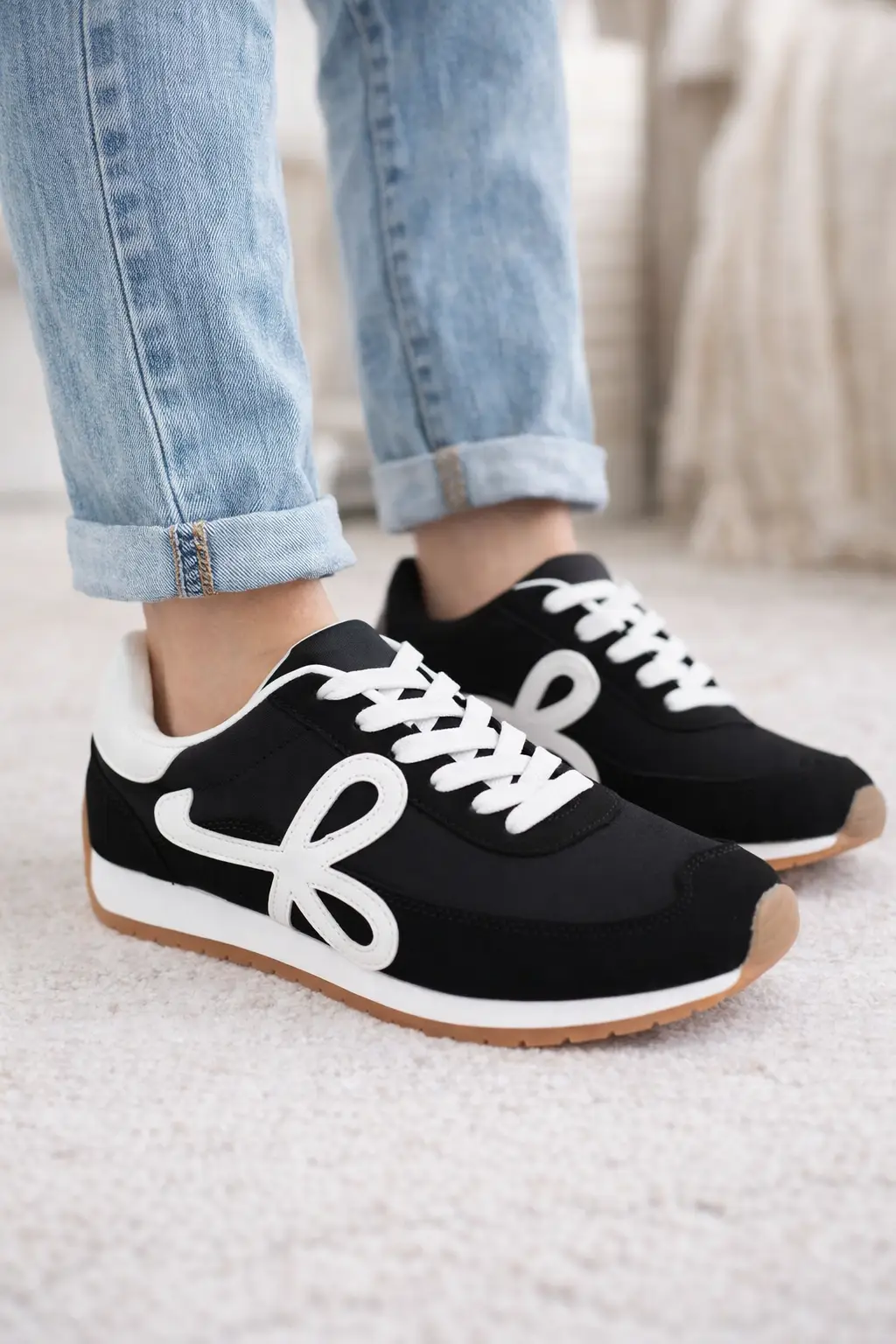 Black retro low top sneakers with white side logo, white laces, and gum sole worn with cuffed blue jeans.
