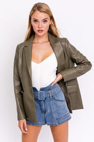 Woman in olive blazer and denim shorts.