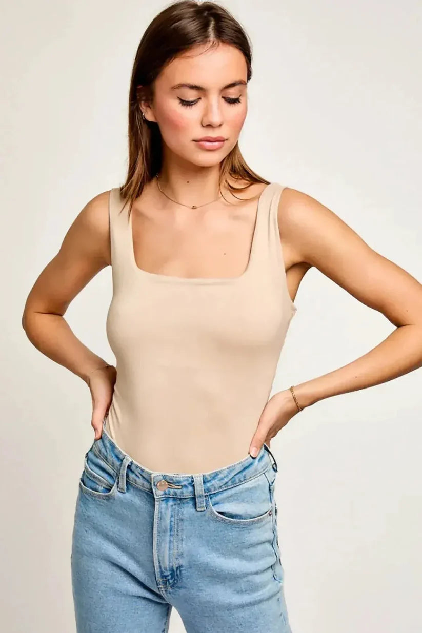 Woman wearing a beige tank top and blue jeans against a plain background