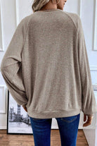 A person wearing a sweater standing next to a wall.