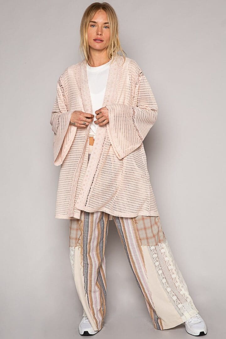 Woman in pink open crochet cardigan and patchwork pants.