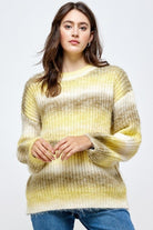 A woman wearing a yellow sweater standing in front of a white wall.