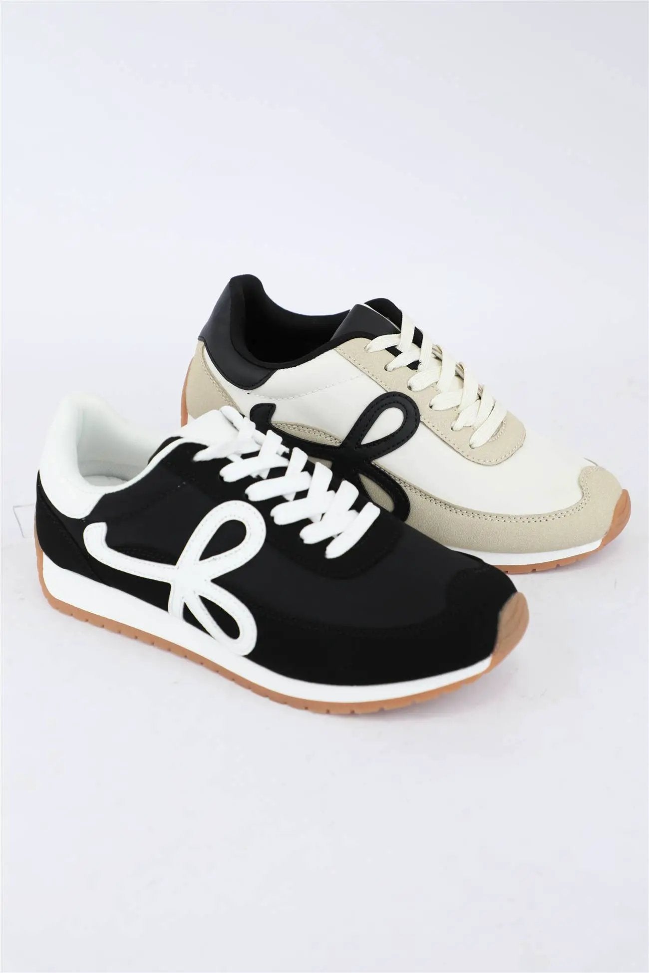 Retro low top sneakers in black and cream featuring distinct loop side accents, white laces, and gum rubber soles for casual wear.