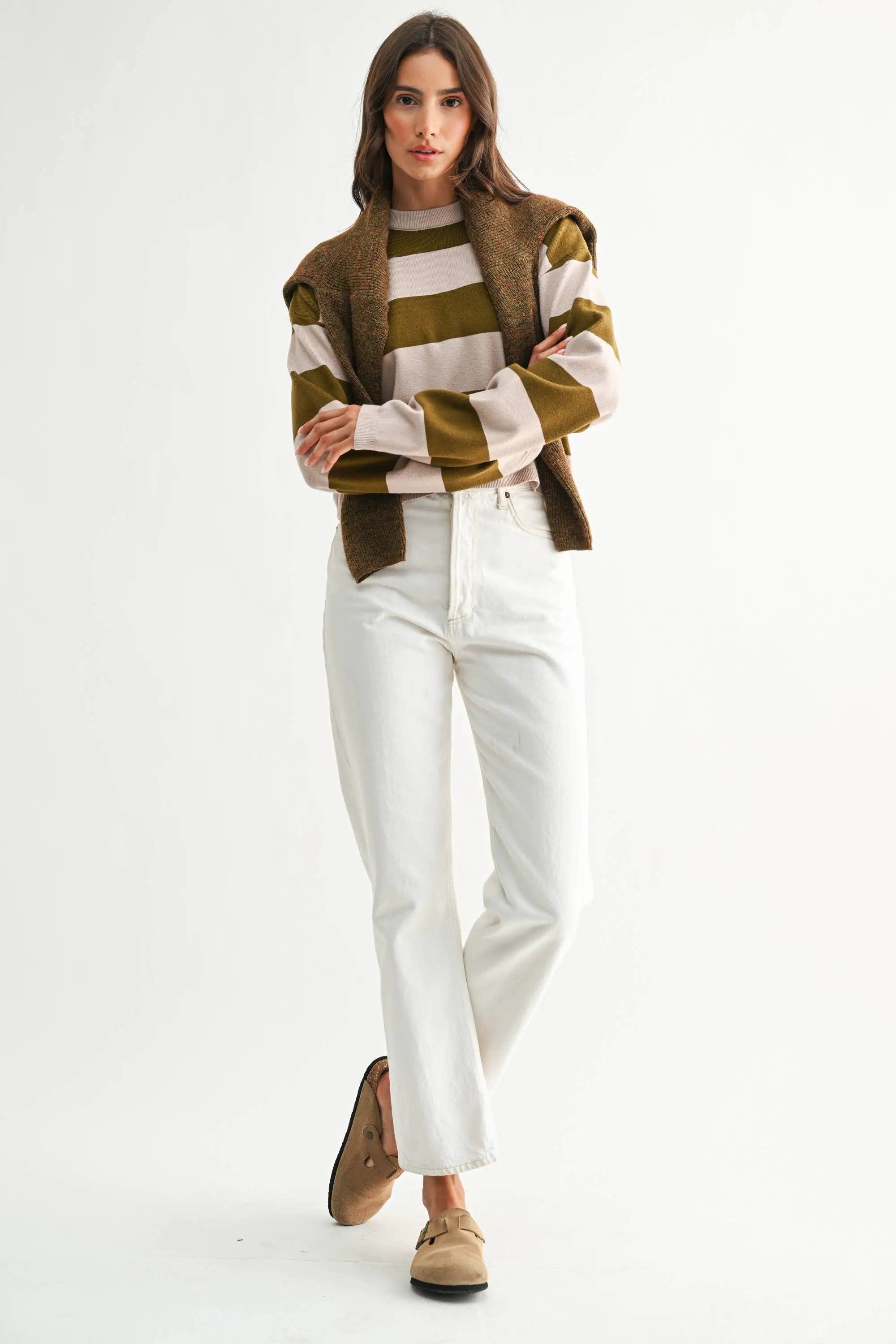 Model wearing taupe and olive bold stripe crewneck sweater with cream stripes, paired with white jeans.
