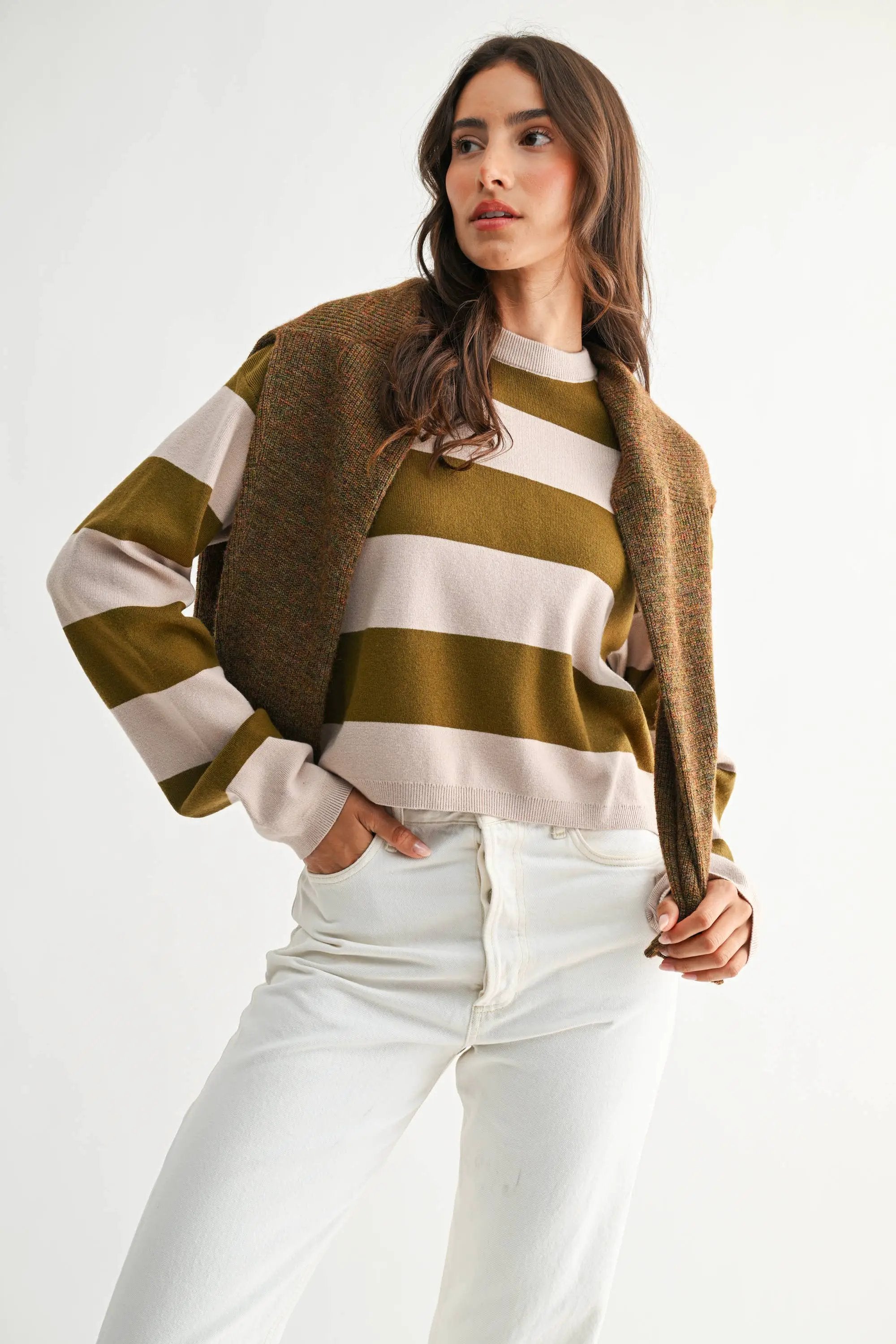 Model in light taupe and olive bold stripe crewneck sweater with a brown tweed coat draped over shoulders.